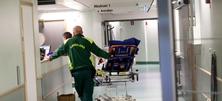 Bild från en sjukhuskorridor där en ambulanspersonal väntar med en bår. 