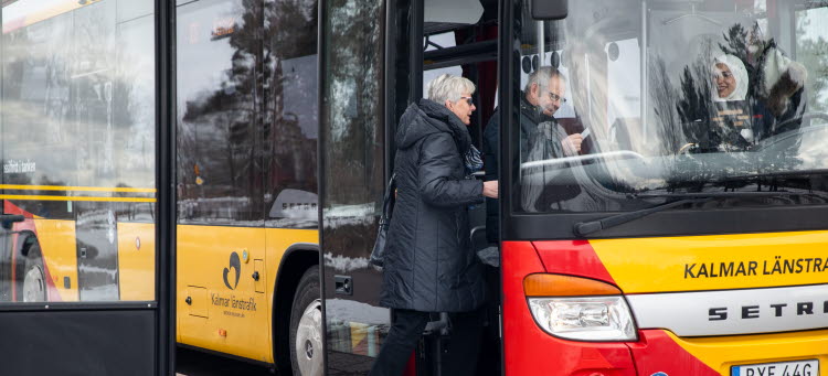 En man och en kvinna kliver ombord på en gul och röd buss. 
