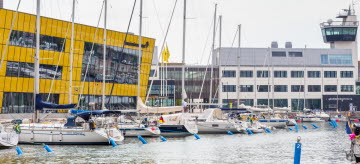 Bild på Linnéuniversitet som ligger i Ölandshamnen. Segelbåtar ligger i vattnet framför universitet.