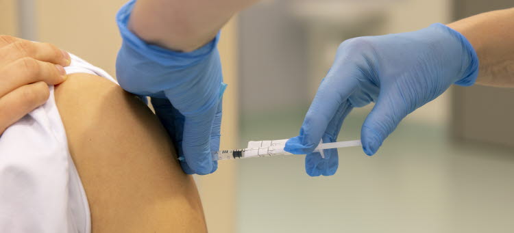 Händer med blå handskar som ger en vaccinationsspruta i överarmen på någon.