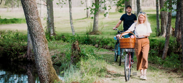 Två personer leder varsin cykel genom en grönskande skog.