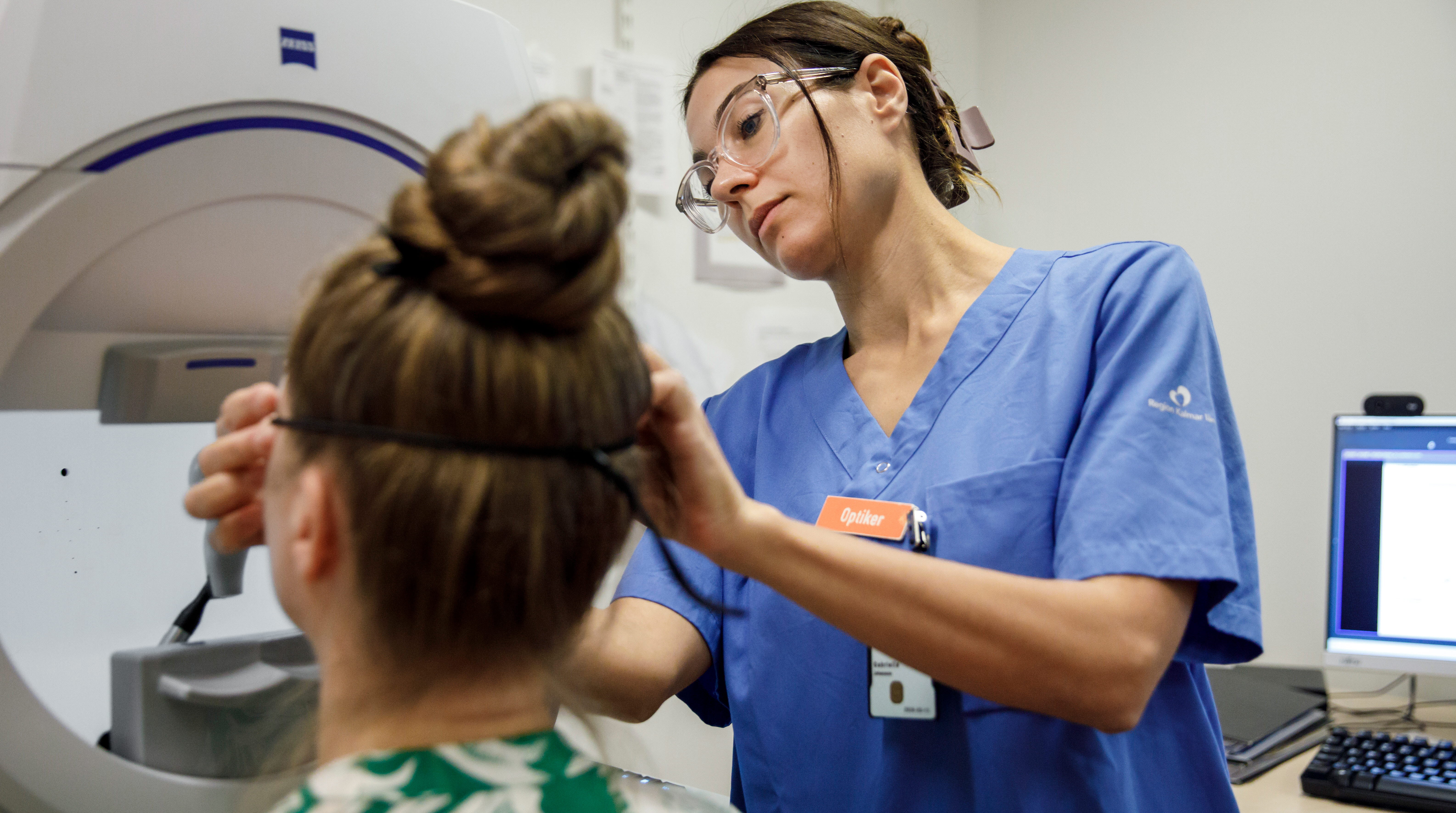 Optikern Gabriella Johansson hjälper patienten inför en undersökning. 