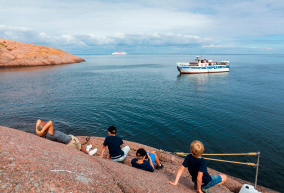 Fyra personer på klipphällar som tittar ut över havet där det kommer in en båt. 