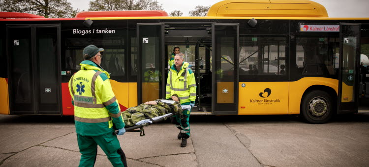 Två ambulanssjukvårdare bär en militär-klädd person på en bår. 