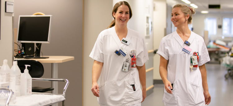 två vårdklädda personer går i en sjukhuskorridor