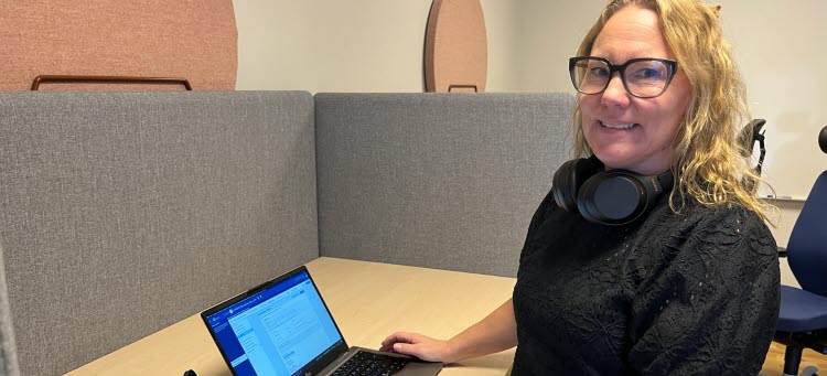 Linda Gustafsson står framför sitt skrivbord med en laptop och tittar in i kameran.