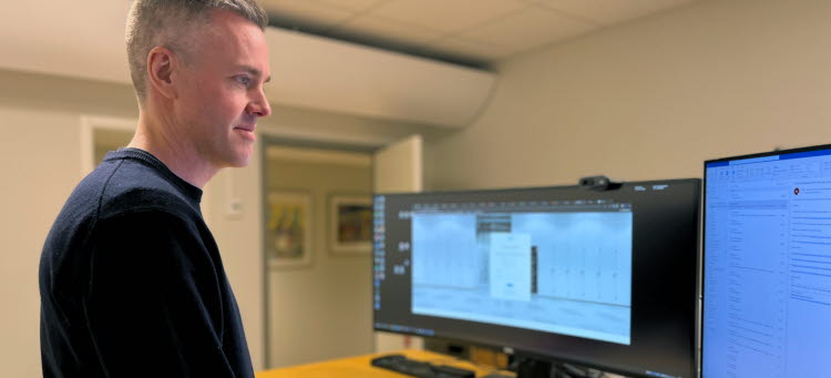 Tobias Söderberg står framför sitt skrivbord och tittar på sina skärmar.
