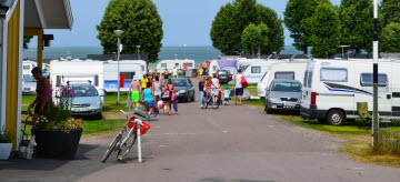 En asfaltsväg ner mot stranden med husvagnar på båda sidorna. Folk går ner mot stranden