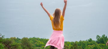 En flicka står på en klippa och sträcker armarna i luften.ften.